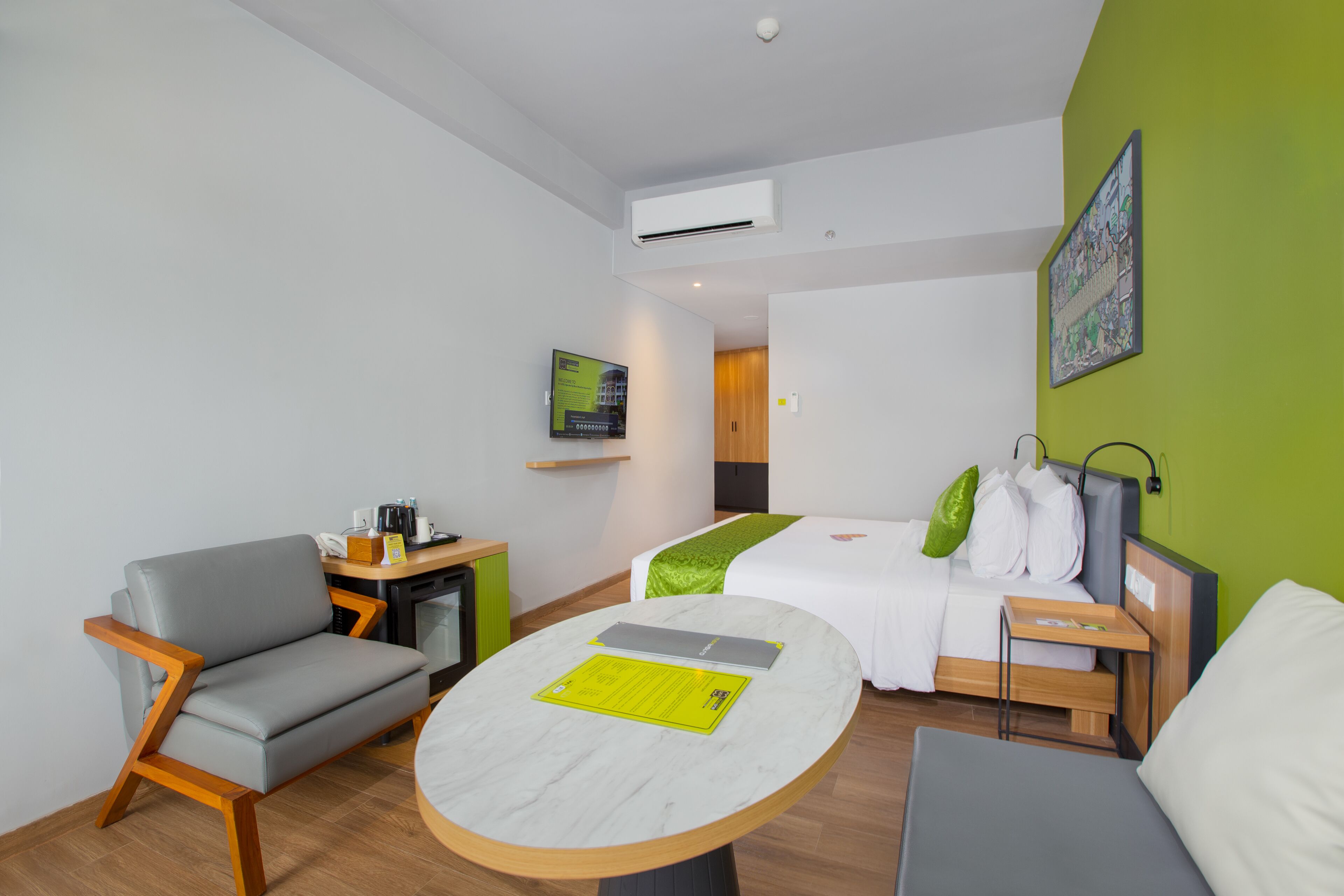 A modern hotel room with a bed, a sofa, a small table, and a desk with a chair.