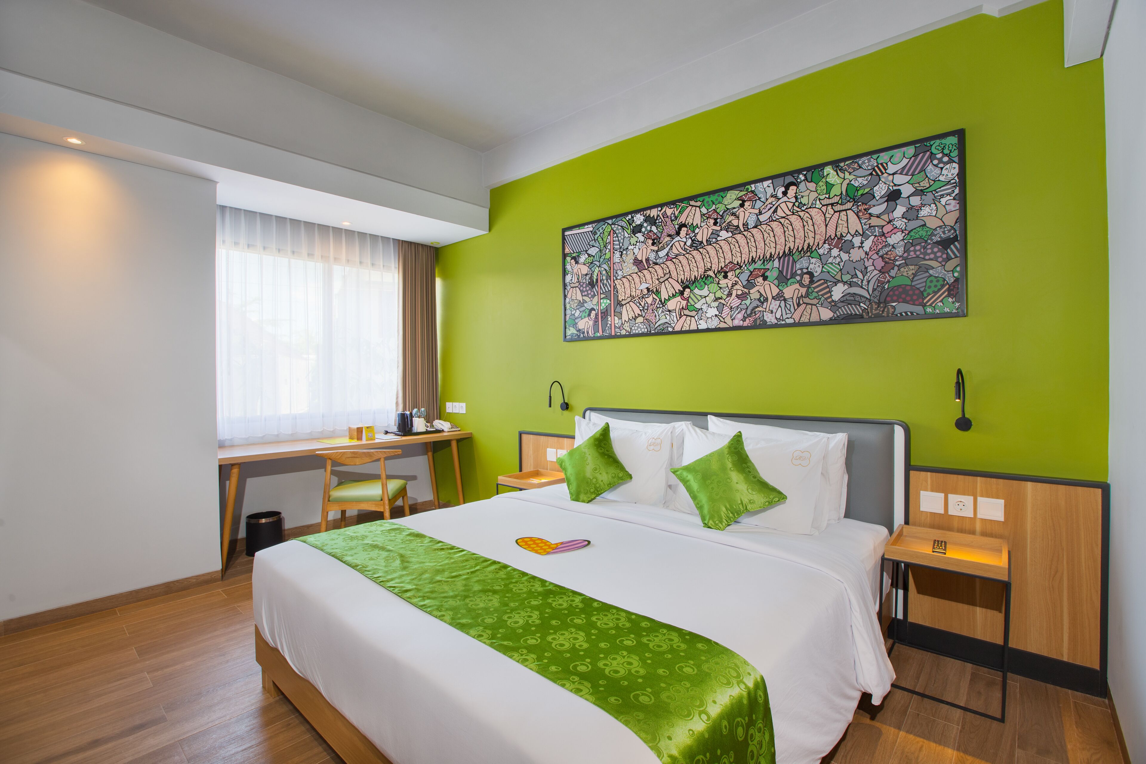 A hotel room with a large bed, green walls, a desk with a chair, and a window with curtains.