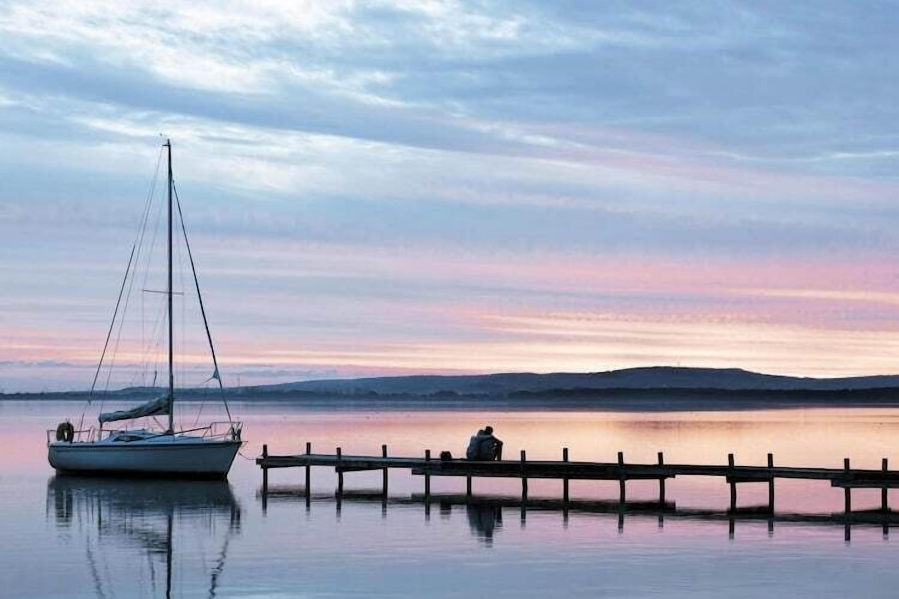Un lago tranquilo con un velero amarrado a un muelle de madera.