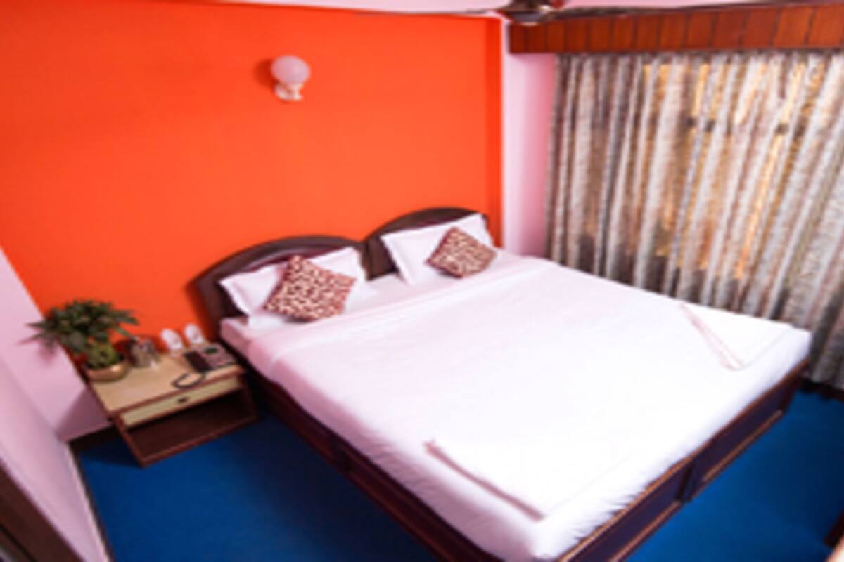 Een slaapkamer met een bed, nachtkastje, televisie en gordijn.