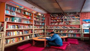 Une bibliothèque avec de nombreuses étagères, une personne qui lit et des espaces de repos avec des sièges rouges.