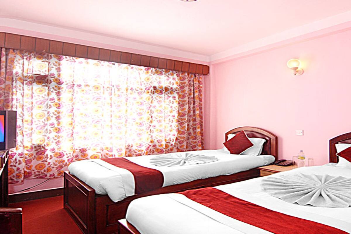 Een hotelkamer met twee bedden, een televisie en een raam met bloemen gordijnen.