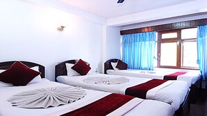 Une chambre d’hôtel avec deux lits simples, un bureau avec une télévision et une fenêtre avec des rideaux bleus.