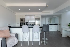 Una cocina moderna con armarios blancos, electrodomésticos de acero inoxidable y una isla central con taburetes de bar.