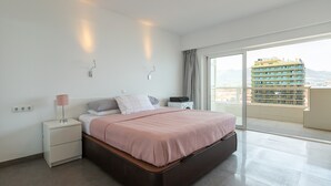 A bedroom with a bed, bedside tables, a lamp, and a view of a building through a large window. - Apartment 'Penthouse with private pool' with Sea View, Wi-Fi and Air Conditioning (Malaga)
