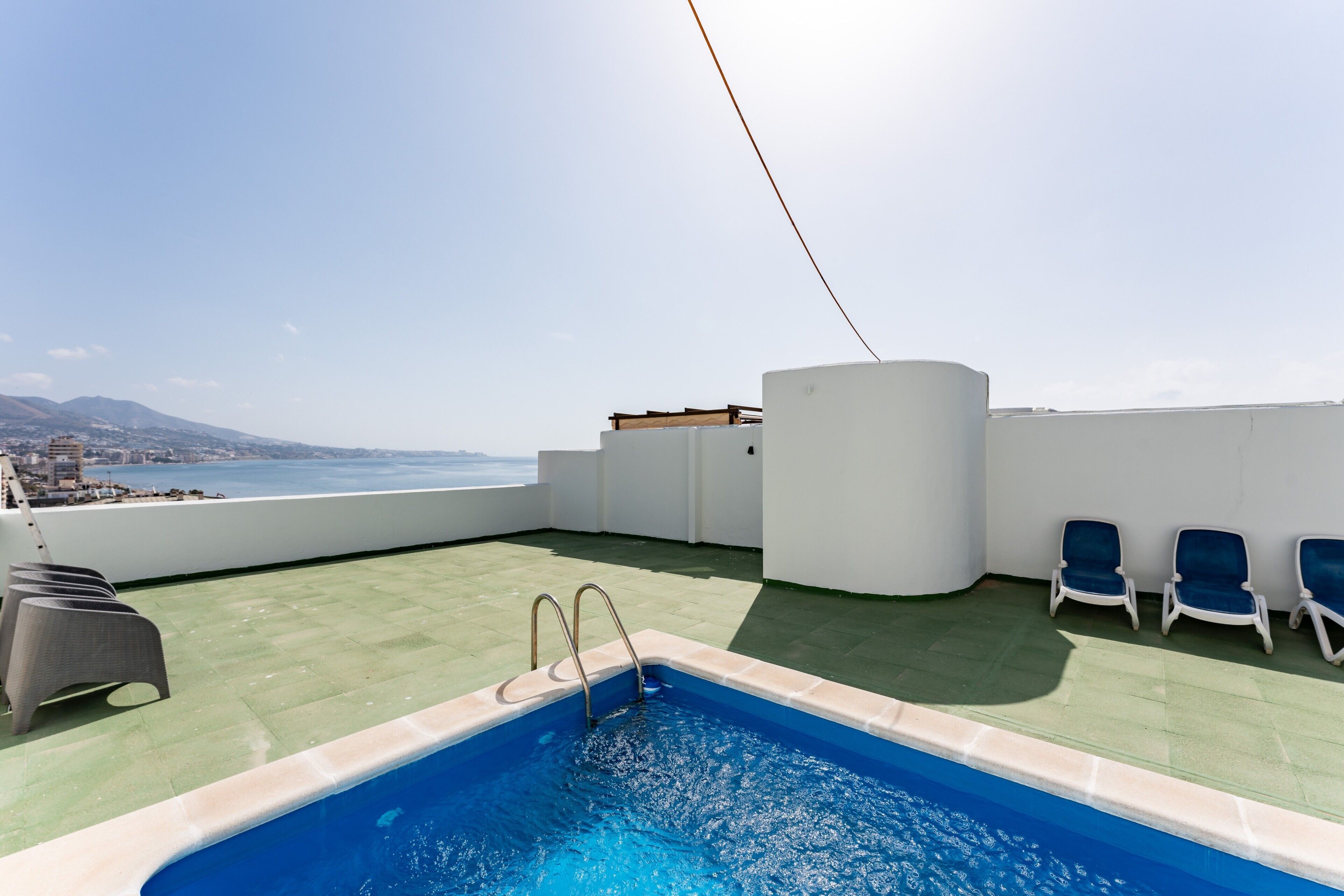 A rooftop pool with a view of the city and mountains, lounge chairs, and a pool ladder.