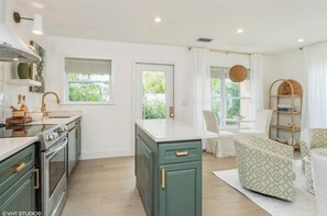 Une cuisine moderne dotée d’un îlot central, d’un four encastré et d’un coin repas avec une chaise et une étagère.