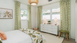 Une chambre à coucher avec un lit, une commode, une lampe et des rideaux.