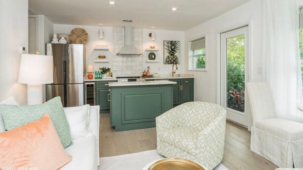 Une cuisine moderne avec des meubles de couleur verte, un îlot central et un coin repas comprenant une table et des chaises blanches.