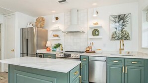 Une cuisine avec des meubles de couleur turquoise, un réfrigérateur en acier inoxydable, une cuisinière à gaz et un lave-vaisselle.