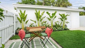 Une terrasse avec une clôture blanche, de l’herbe verte et un mur blanc orné de plantes.