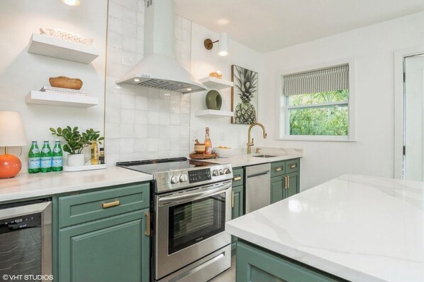 Une cuisine moderne avec des meubles blancs et verts, des appareils en acier inoxydable et une fenêtre donnant sur un paysage verdoyant.