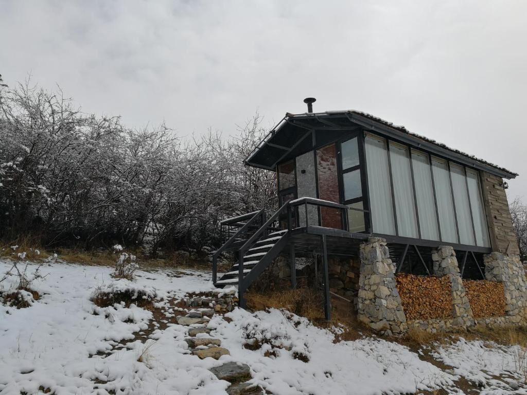 A stone building with a metal staircase leading to a door, surrounded by snow-covered ground and trees.