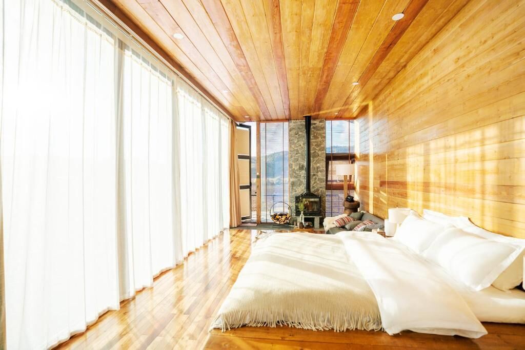 A spacious bedroom with a large bed, wooden ceiling, and a stone fireplace.