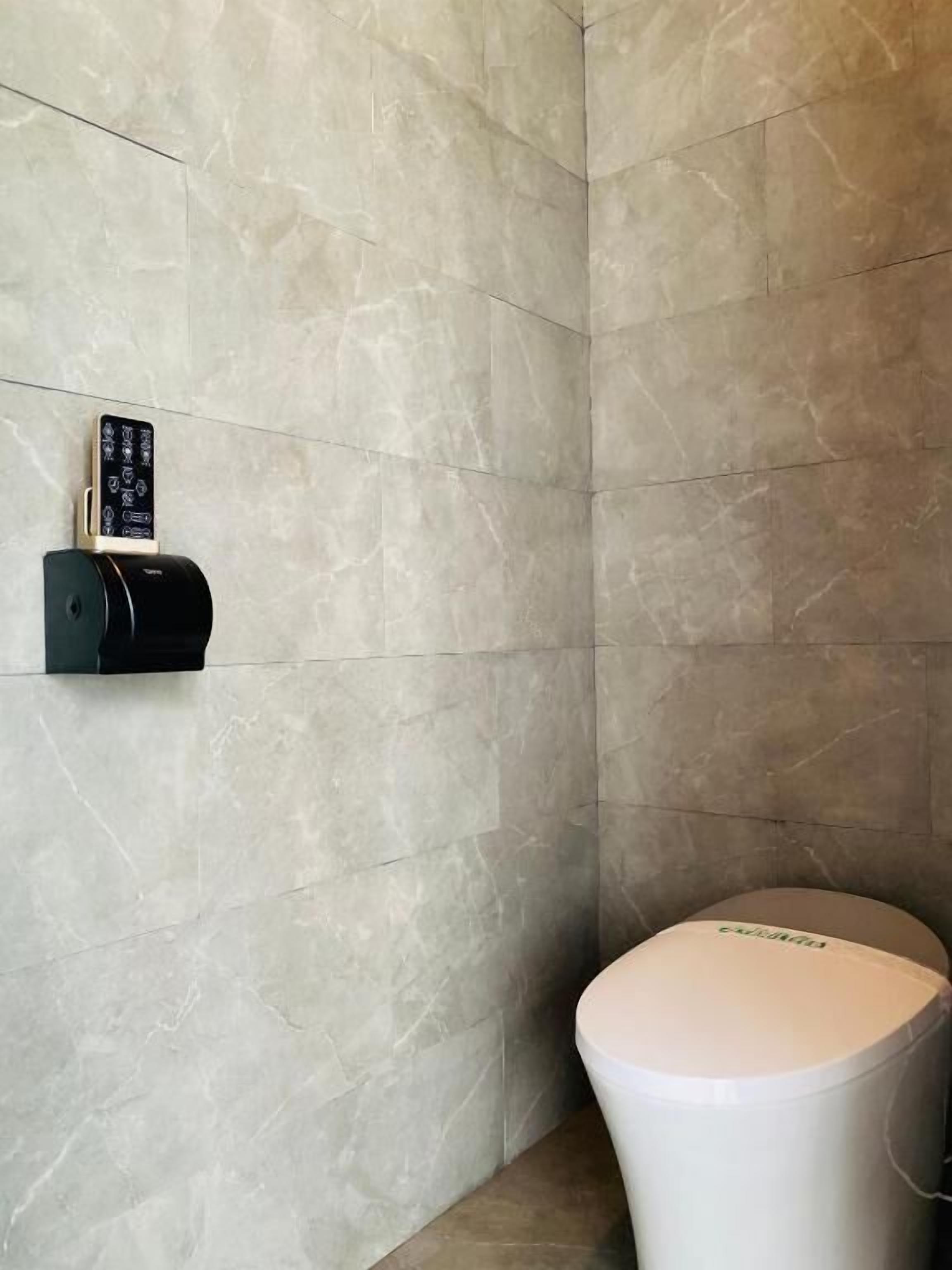 A bathroom with a toilet, a wall-mounted toilet paper dispenser, and a hand sanitizer dispenser.