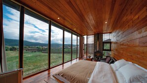 Ruime slaapkamer met een groot bed, houten wanden en uitzicht op een groen landschap door grote ramen.