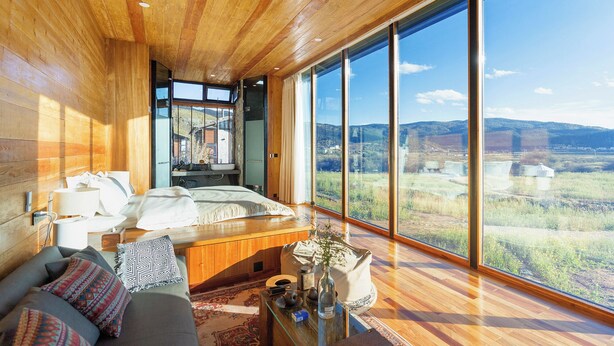 Een moderne slaapkamer met een groot raam, houten plafond en uitzicht op een landschap.