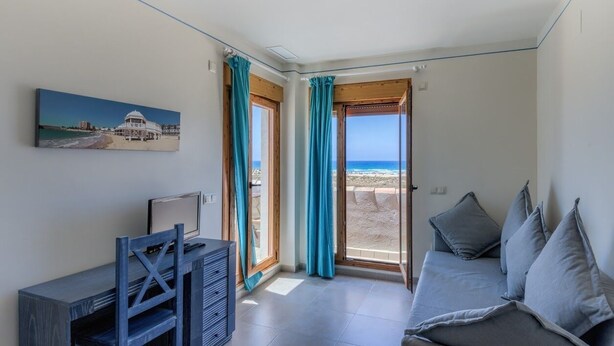 Une chambre avec un bureau, un lit et une vue sur la plage, visible à travers une porte vitrée.