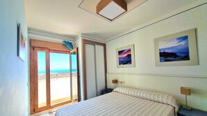 Une chambre avec un lit, une table de chevet, une lampe fixée au mur et une porte donnant sur un balcon avec vue sur la plage.