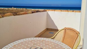 Un balcon avec une table carrelée et une chaise en osier, donnant sur une plage.