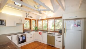 A modern kitchen with white cabinets, stainless steel appliances, and wooden flooring. - 20 Yarrong Rd - a very large house split over three levels (Point Lookout)