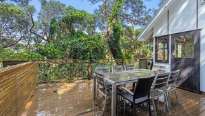 An outdoor deck with a table and chairs, surrounded by lush greenery and trees. - 20 Yarrong Rd - a very large house split over three levels (Point Lookout)