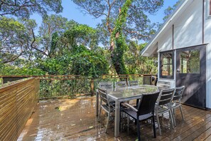 An outdoor deck with a table and chairs, surrounded by lush greenery and trees. - 20 Yarrong Rd - a very large house split over three levels (Point Lookout)