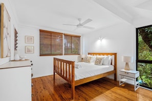 A bedroom with a wooden bed, white bedding, a bedside table with a lamp, and a window with blinds. - 20 Yarrong Rd - a very large house split over three levels (Point Lookout)