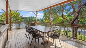 A covered outdoor area with a table and chairs, surrounded by a wooden deck and metal railings, overlooking a road and greenery. - 20 Yarrong Rd - a very large house split over three levels (Point Lookout)
