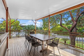 A covered outdoor area with a table and chairs, surrounded by a wooden deck and metal railings, overlooking a road and greenery. - 20 Yarrong Rd - a very large house split over three levels (Point Lookout)