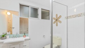 A bathroom with a glass shower enclosure, a toilet, a sink with a mirror, and a window above the sink. - 20 Yarrong Rd - a very large house split over three levels (Point Lookout)