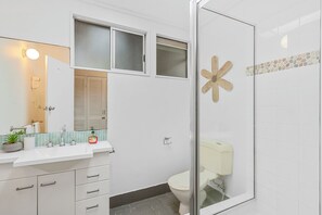 A bathroom with a glass shower enclosure, a toilet, a sink with a mirror, and a window above the sink. - 20 Yarrong Rd - a very large house split over three levels (Point Lookout)