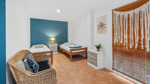 A bedroom with two beds, a wicker chair, a bedside table with a lamp, a small plant, and a wall-mounted macrame piece. - 20 Yarrong Rd - a very large house split over three levels (Point Lookout)