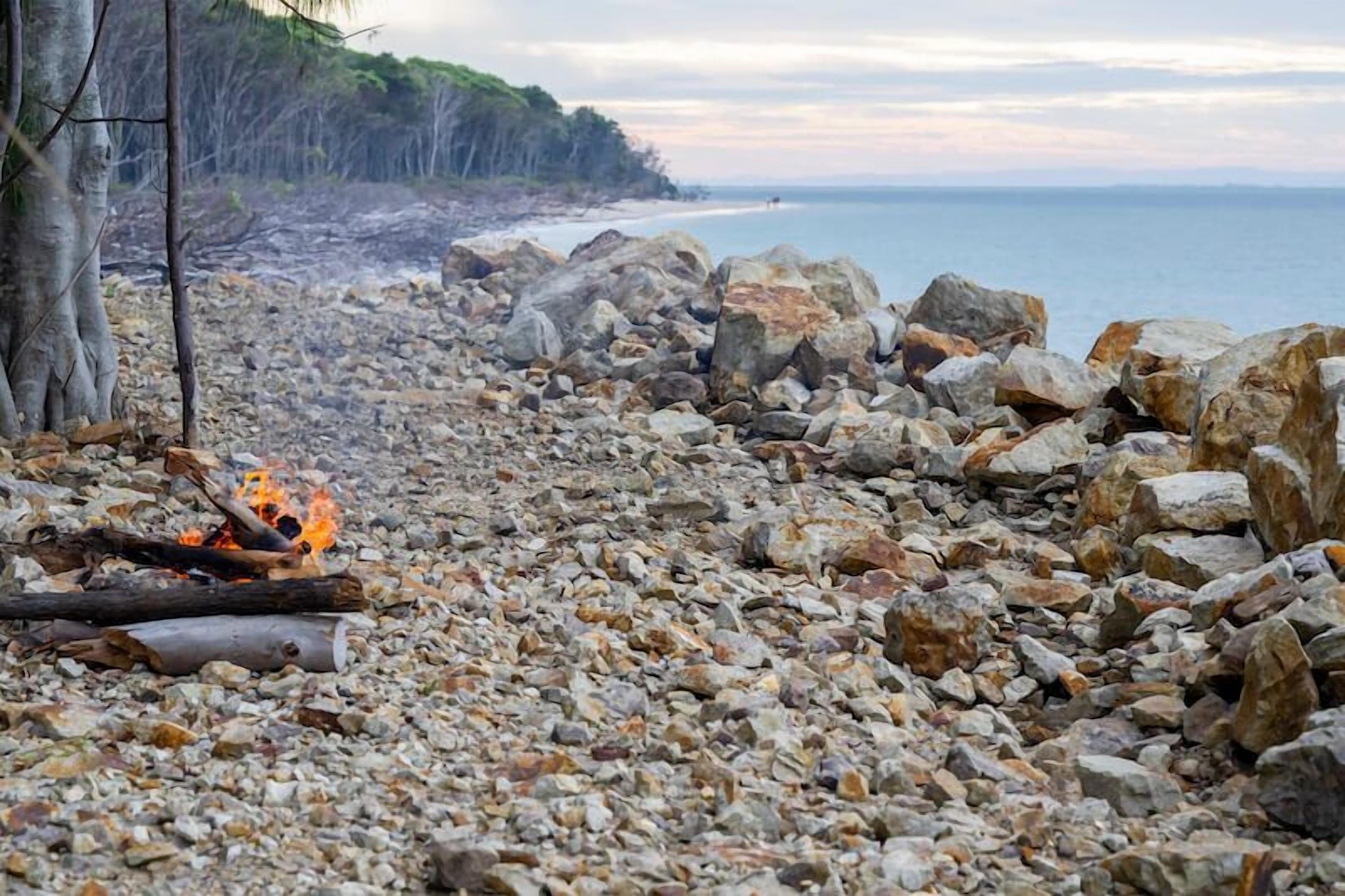 A rocky beach with a fire and a view of the sea.
