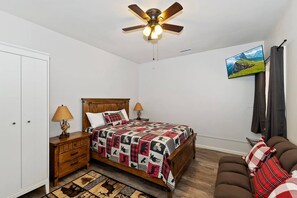 Un dormitorio con una cama, mesitas de noche, ventilador de techo, televisión y un sofá.