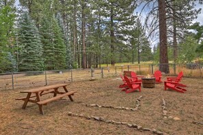 Un área de picnic con un banco de madera y sillas Adirondack rojas, rodeada por una cerca y árboles.