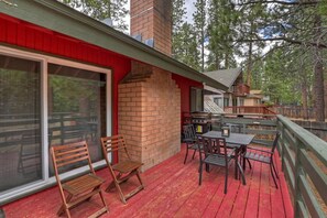 Una terraza de madera con mobiliario exterior, una chimenea de ladrillo y un ventanal que da a un espacio interior.