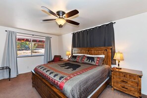A bedroom with a bed, a nightstand, a ceiling fan, a window with curtains, and a view outside.