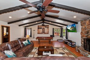 A spacious living room with a leather sofa, a pool table, a ceiling fan, and a stone fireplace. - The Ginger Lodge By Destination Big Bear: Walking Distance to Meadow Park! Spa! Close to Snow Summit! Pool Table! (Big Bear Lake)