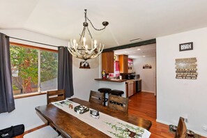 Un comedor con candelabro, mesa de madera y sillas. Se ve una cocina al fondo.
