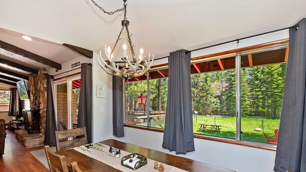 A dining area with a wooden table, chandelier, and large windows overlooking a garden.