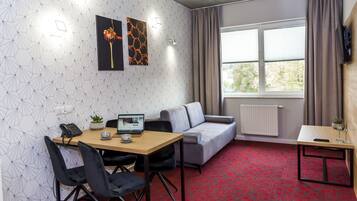Una habitación moderna con un muro estampado con un diseño geométrico, un sofá gris, una mesa de madera con un ordenador portátil y una alfombra roja.