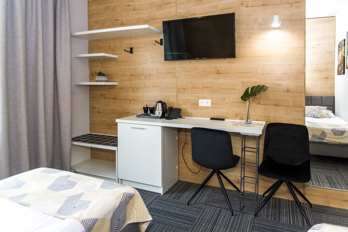 A modern hotel room with a bed, a desk with a chair, a TV, and a small plant.