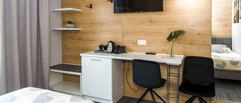 Una habitación de hotel moderna con una cama, un escritorio con una silla, un televisor y una planta pequeña.