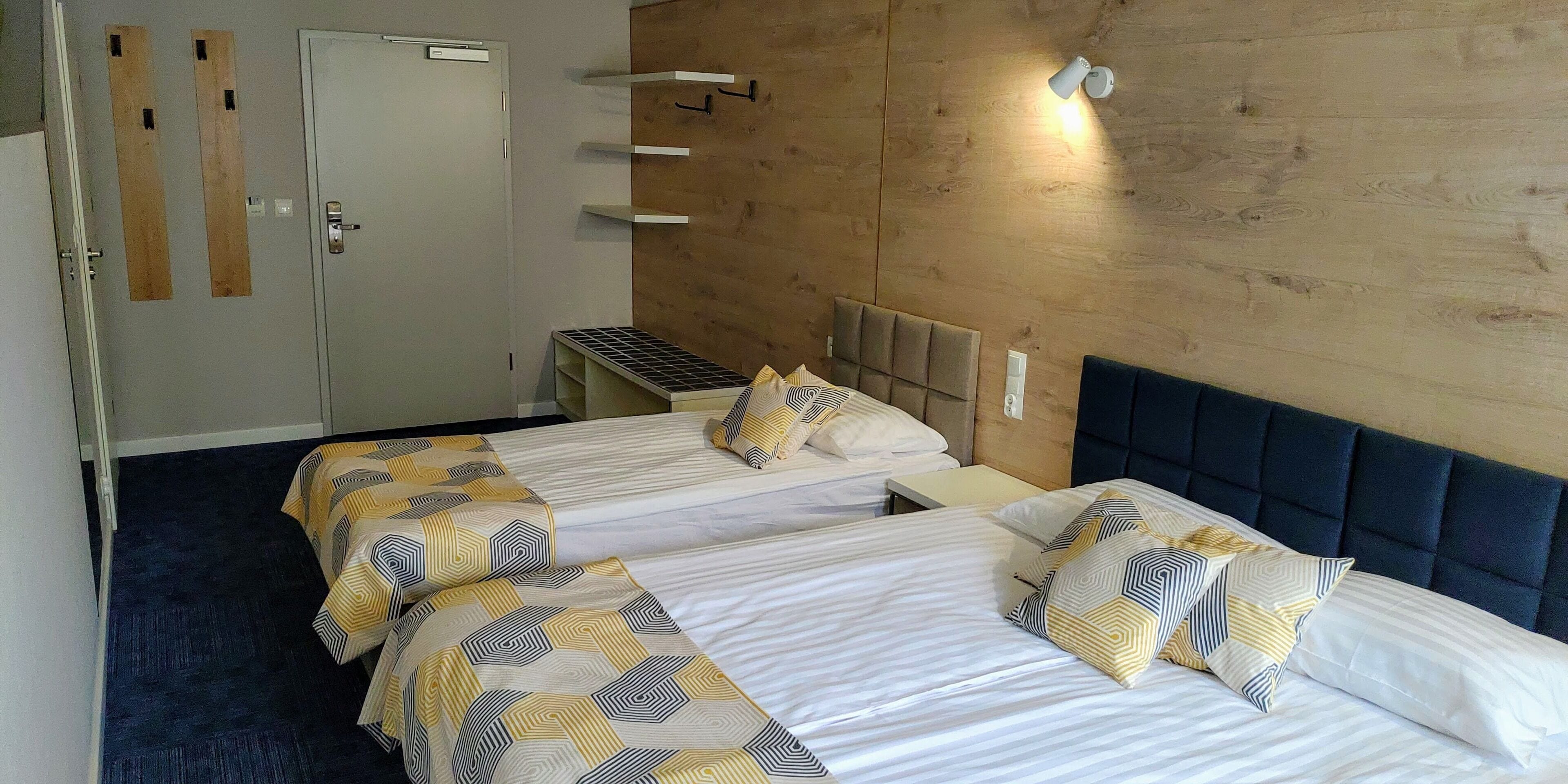 Hotellihuone, jossa on kaksi sänkyä, puinen seinä, pieni työpöytä ja vaatekaappi.