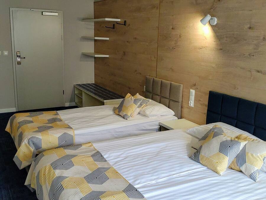 Hotellihuone, jossa on kaksi sänkyä, puinen seinä, pieni työpöytä ja vaatekaappi.