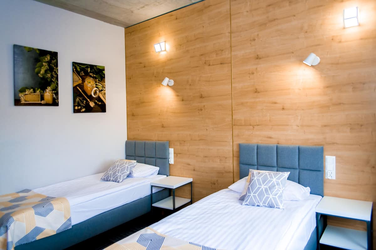 A hotel room with two single beds, wooden panel walls, and two wall-mounted light fixtures.