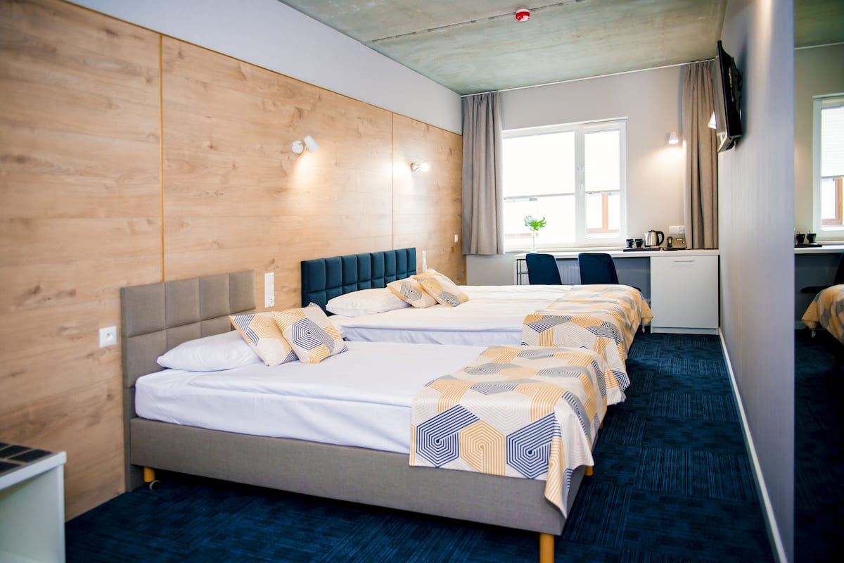 A hotel room with two beds, a desk, and a window with curtains.
