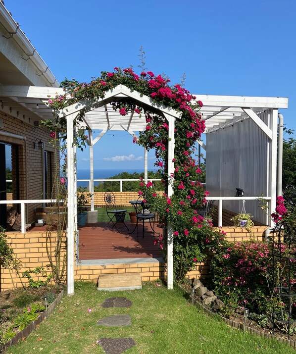 A covered patio with a pergola adorned with pink flowers, a brick wall, and a view of the ocean.