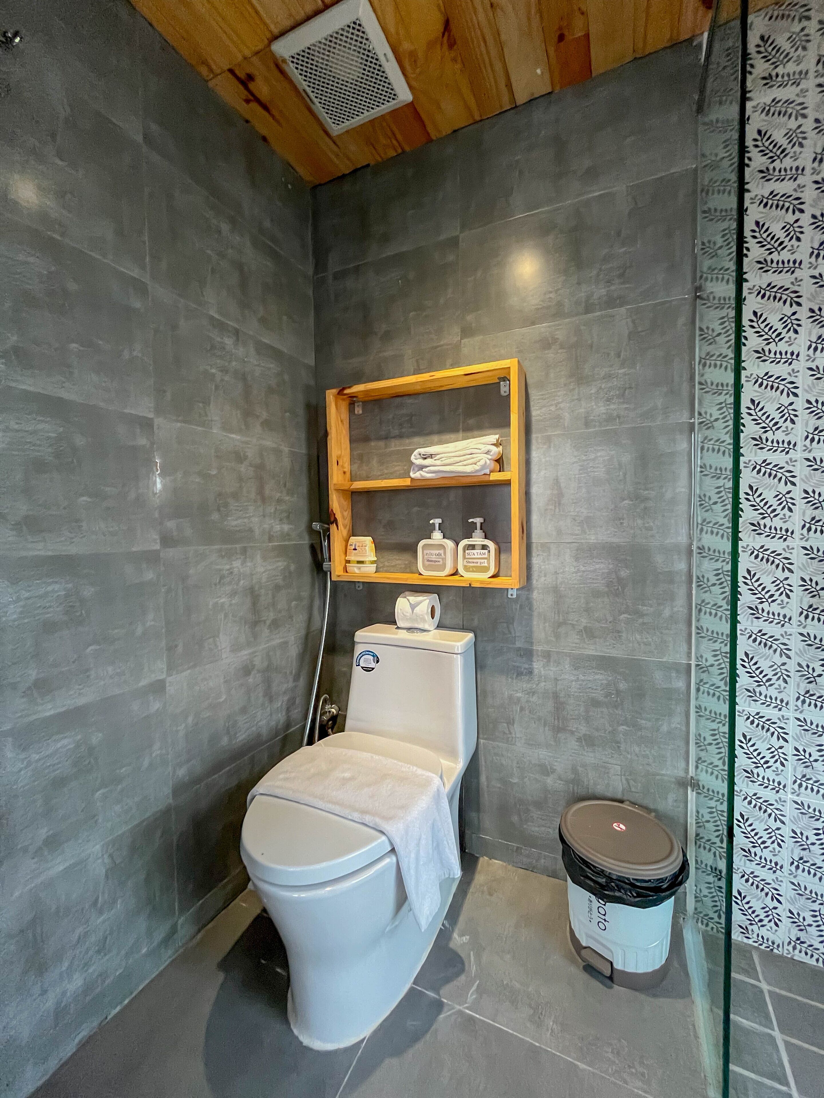 A modern bathroom with a toilet, a shower, and a small shelf with toiletries.